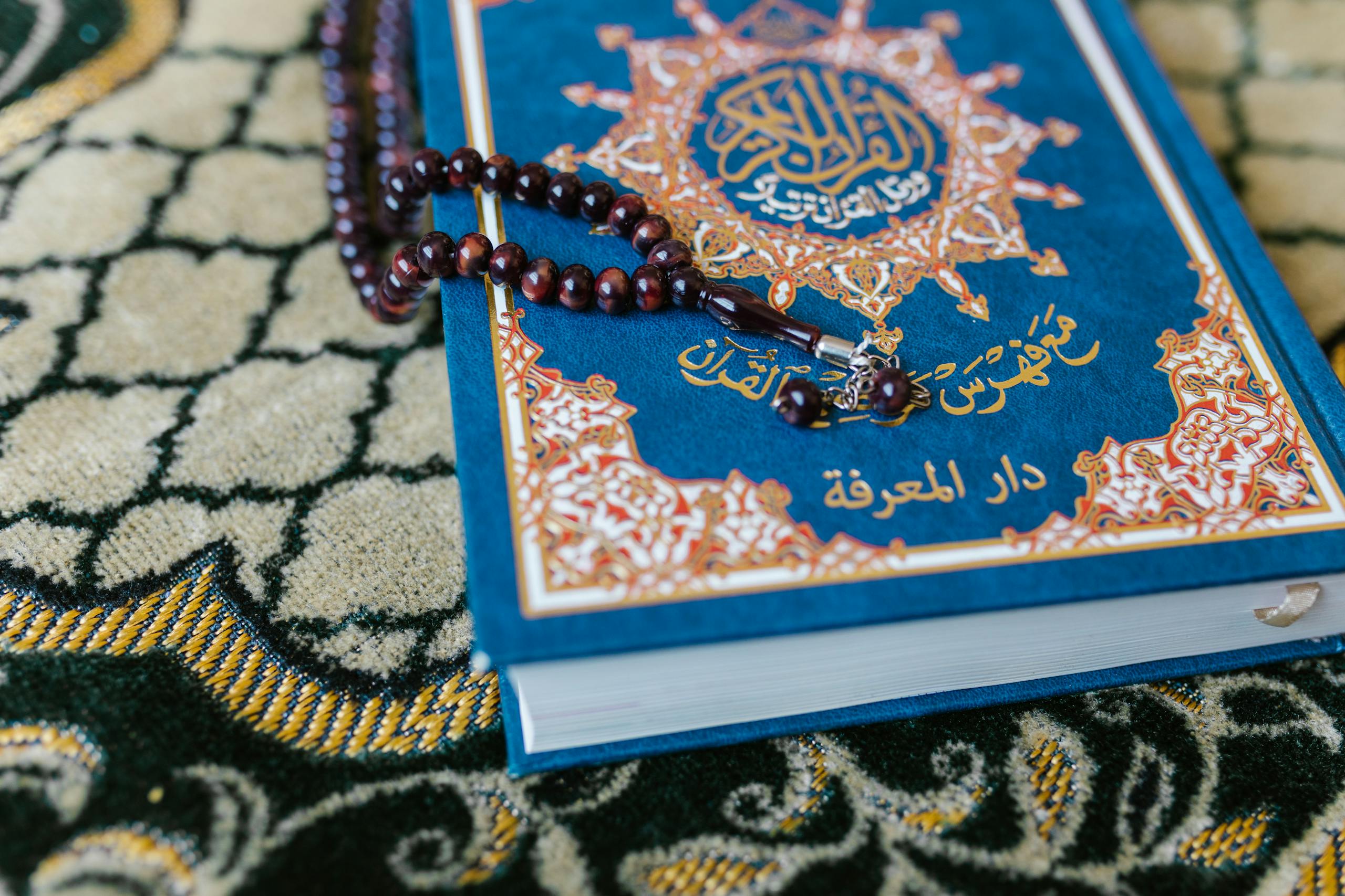 A Quran with prayer beads on a decorative carpet, symbolizing Islamic spirituality.