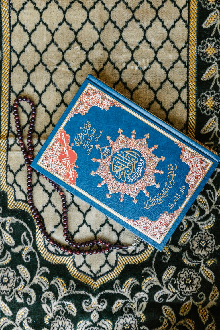 Top view of a Quran with prayer beads on a decorative Islamic carpet.